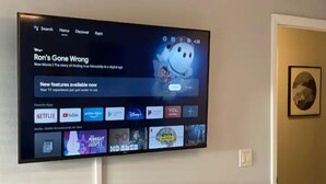 Un televisor montado en la pared mostrando una interfaz de servicio de transmisión con varios iconos de aplicaciones y el título de una película.
