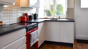 Una cocina moderna con armarios blancos, una estufa roja y una ventana que ofrece vistas a árboles.