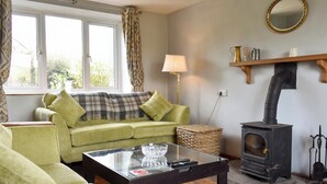 Una sala de estar acogedora con un sofá verde, una mesa de centro de vidrio, una chimenea y un ventanal con cortinas.