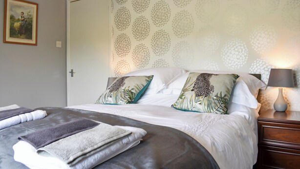 Una cama bien hecha con una manta gris y blanca, un cojín estampado de leopardo y una pared con diseño.
