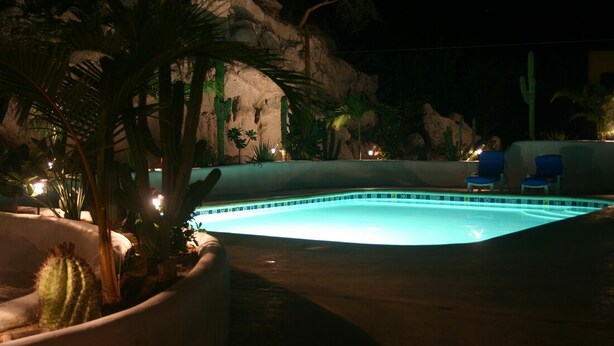 A swimming pool with a rock wall backdrop, surrounded by palm trees and cacti. - Las BouganVillas 2 or 3 Bd Poolside Homes (Los Barriles)
