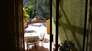 A view through a sliding glass door to an outdoor patio area with a pool, a table, and chairs. - Las BouganVillas 2 or 3 Bd Poolside Homes (Los Barriles)
