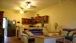 A cozy living room with a sofa, a coffee table, and a kitchen area with wooden cabinets and a refrigerator. - Las BouganVillas 2 or 3 Bd Poolside Homes (Los Barriles)