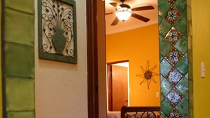 A hallway with a tiled floor, a ceiling fan, a bed with a white bedspread, and a decorative wall panel. - Las BouganVillas 2 or 3 Bd Poolside Homes (Los Barriles)