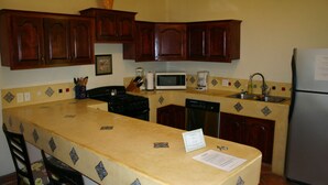 A kitchen with wooden cabinets, a microwave, a stove, a dishwasher, and a refrigerator. - Las BouganVillas 2 or 3 Bd Poolside Homes (Los Barriles)