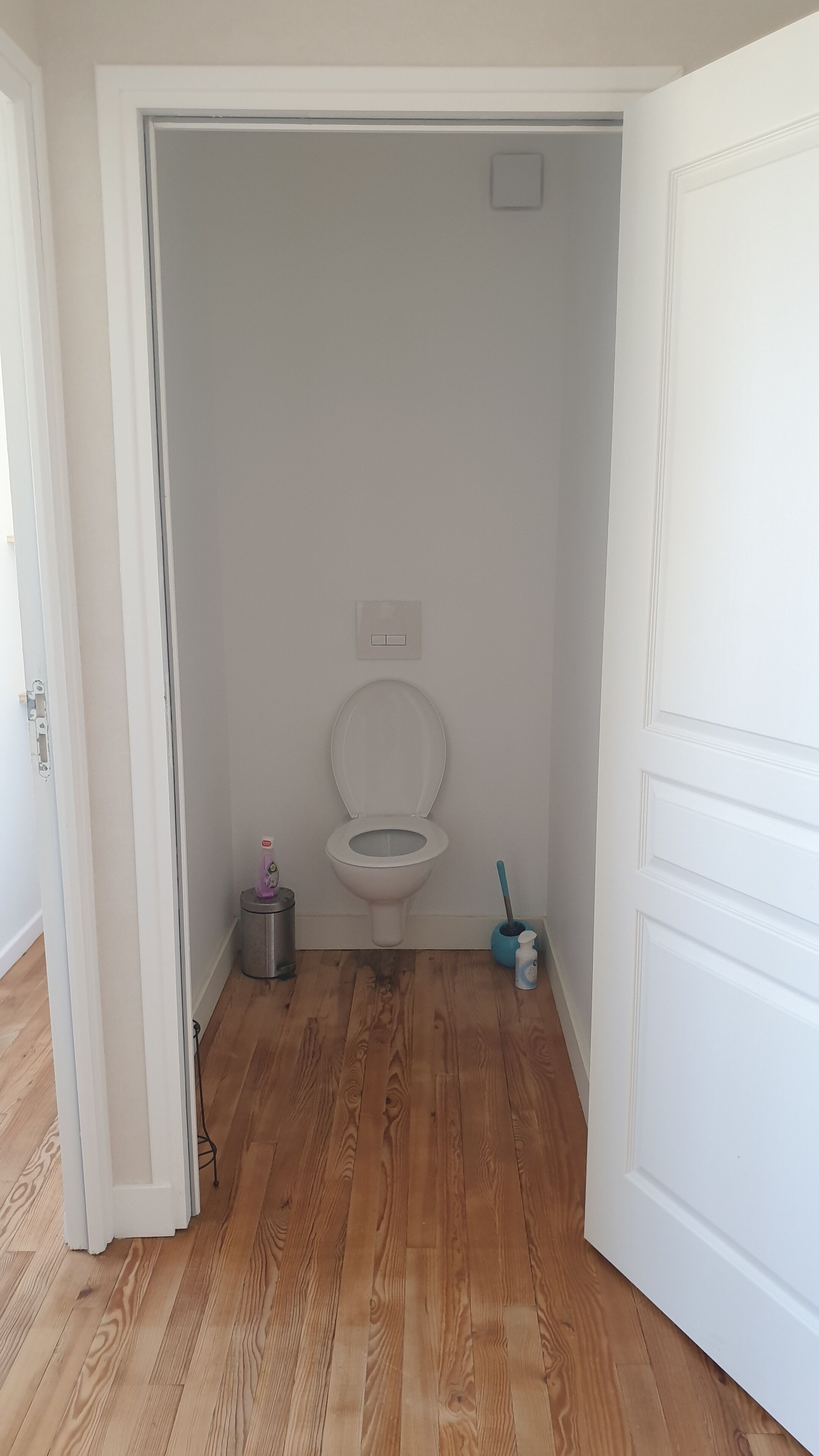 Un baño pequeño y estrecho con un inodoro blanco, un cubo de basura y un balde de limpieza.