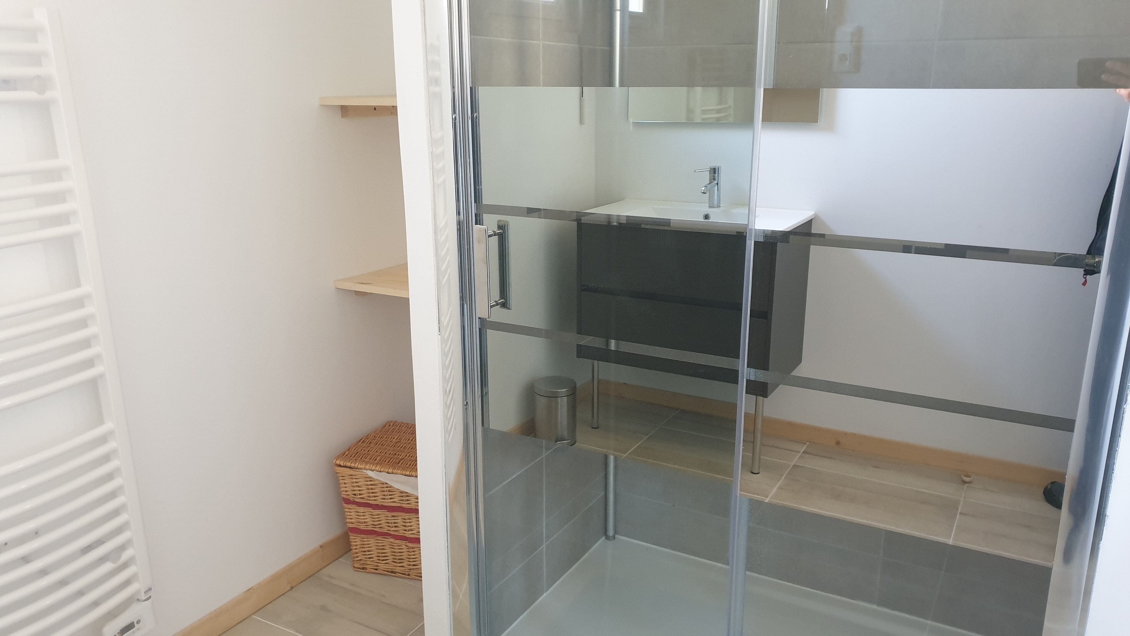 Un bagno con cabina doccia in vetro, lavandino bianco e piccolo cestino.