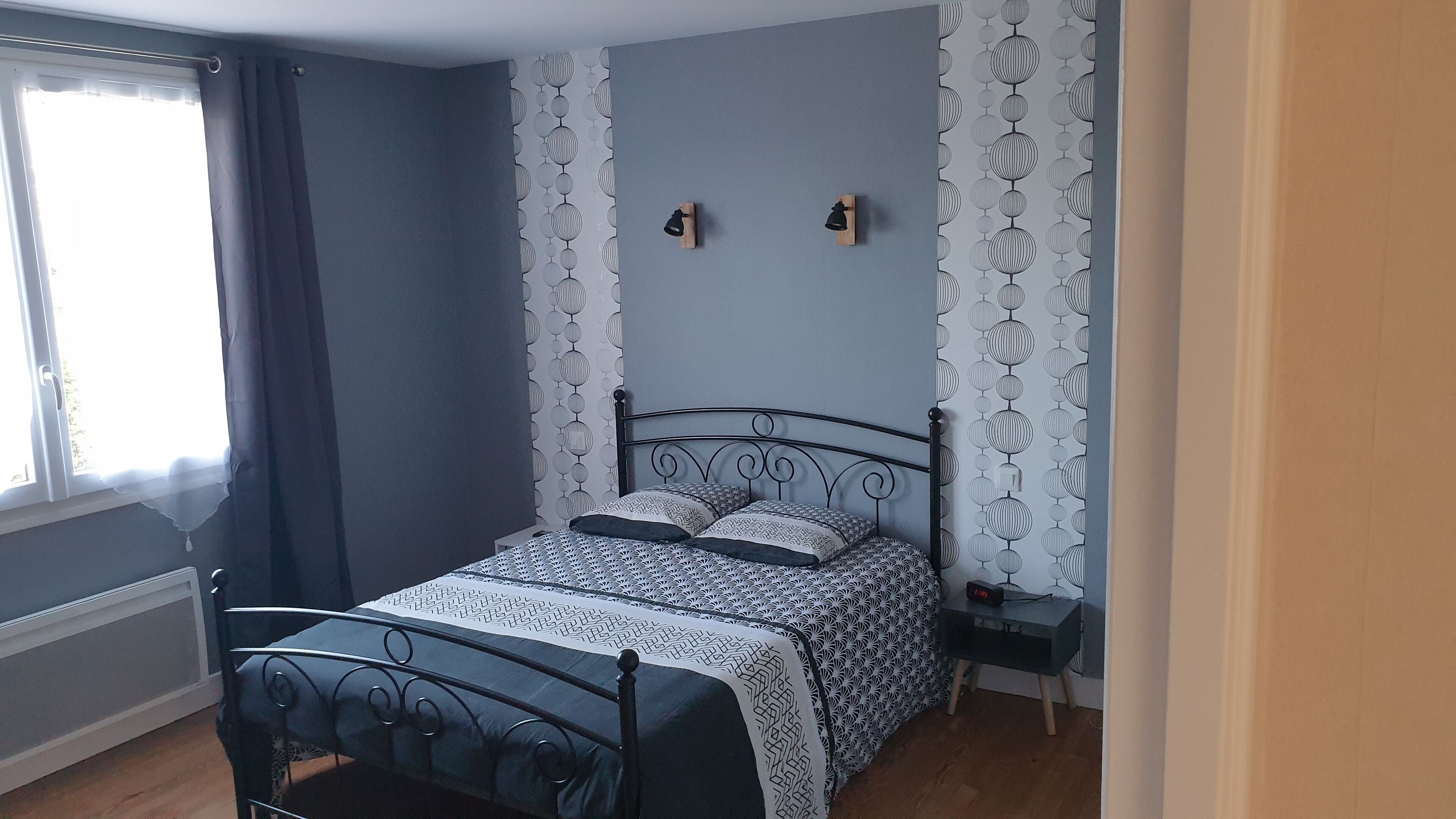 Une chambre à coucher avec un lit, une table de chevet, une horloge murale et une fenêtre avec des rideaux.