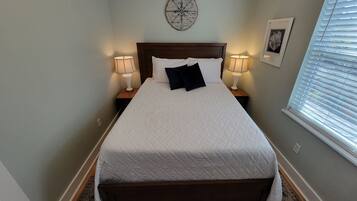 A neatly made bed with white bedding and two pillows, flanked by bedside tables with lamps, a compass wall decoration, and a framed picture.