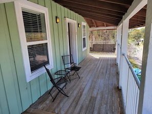 A covered porch with a wooden floor, two metal chairs, and a bench.