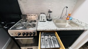 A kitchen with a stove, oven, toaster, sink, and drawer with utensils.