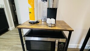 A kitchen area with a microwave, a coffee maker, and a paper towel dispenser on a wooden table.
