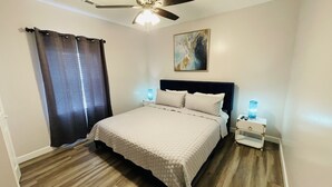 A bedroom with a bed, a ceiling fan, a nightstand, and a painting on the wall.