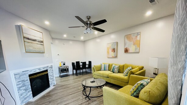 A living room with a fireplace, yellow sofa, dining table, and ceiling fan.