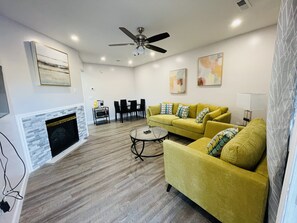 A living room with a fireplace, yellow sofa, dining table, and ceiling fan. - Entire condominium in the center of Pigeon Forge<br>210 (Pigeon Forge)