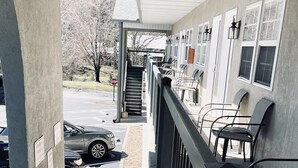 A covered outdoor area with a staircase leading to a building entrance, outdoor seating, and a parked car.