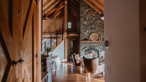 Un interior de madera con chimenea de piedra, una escalera y sillones de cuero.