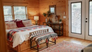 Un dormitorio acogedor de cabaña de madera con cama, banco, escritorio y una puerta que da al exterior.