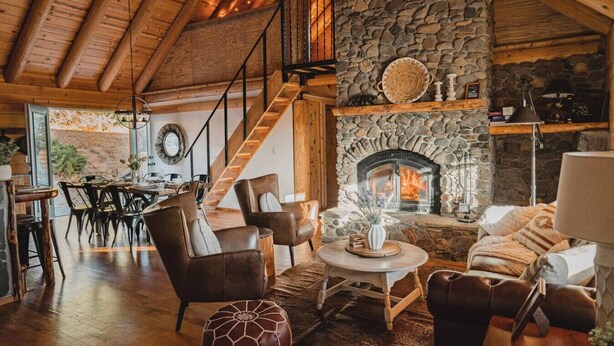 Una sala de estar acogedora con chimenea de piedra, vigas de madera en el techo y una escalera que conduce a un nivel superior.