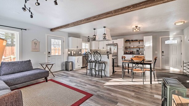 Un vaste espace de vie comprenant un canapé gris, un tapis rouge et beige, ainsi qu’une table à manger avec des chaises.