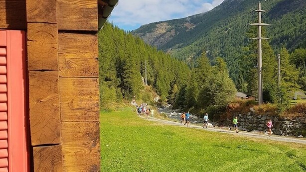Een houten gebouw met een rode deur, een geparkeerde auto en uitzicht op een berg en een pad met mensen.