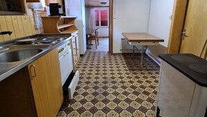 Een kleine keuken met houten kastjes, een vloer met een patroon, en uitzicht op een eetgedeelte.