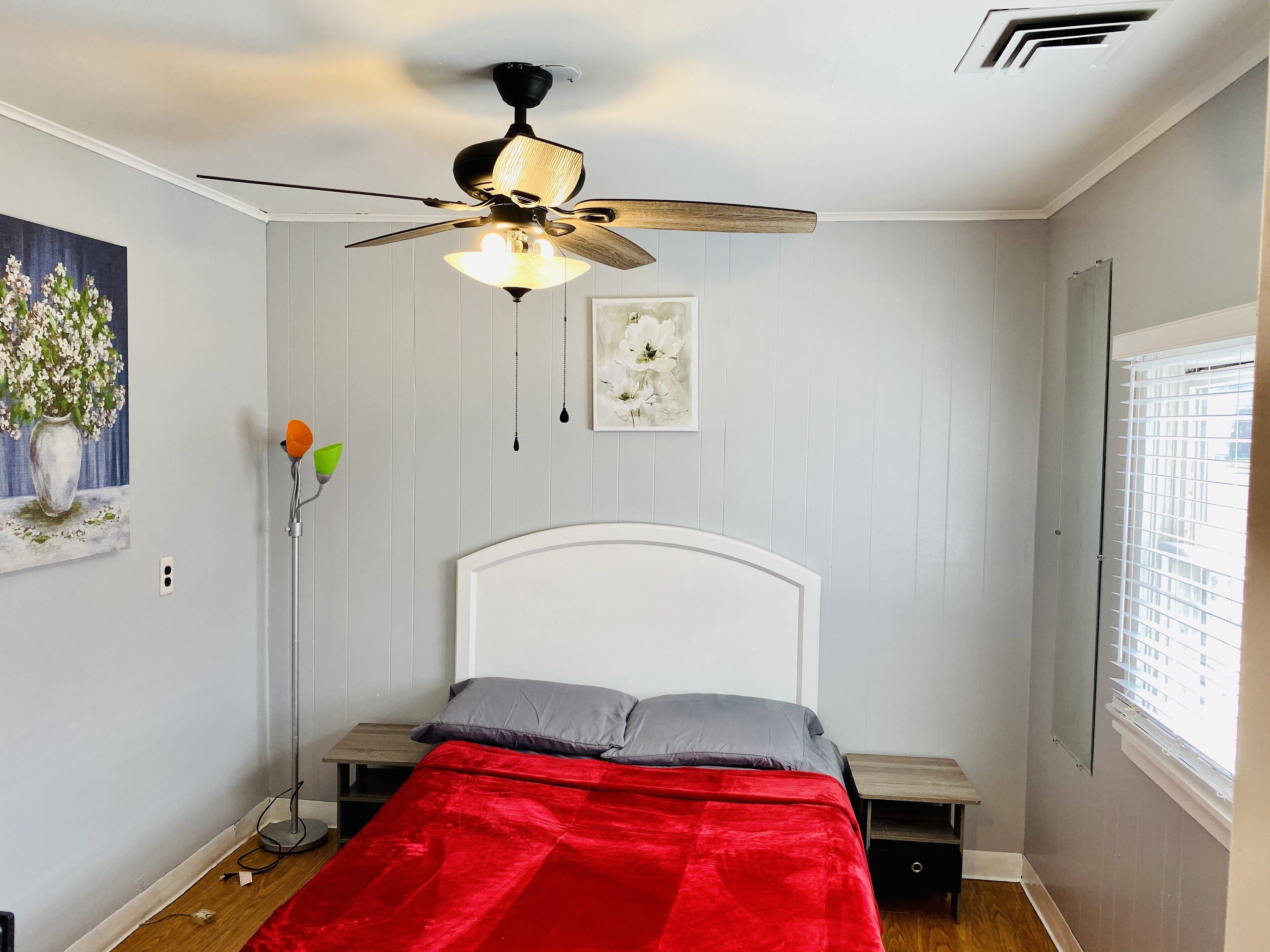 A bedroom with a bed, a ceiling fan, a window with blinds, and a painting on the wall.