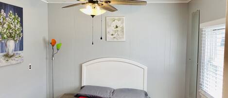 A bedroom with a bed, a ceiling fan, a window with blinds, and a painting on the wall.