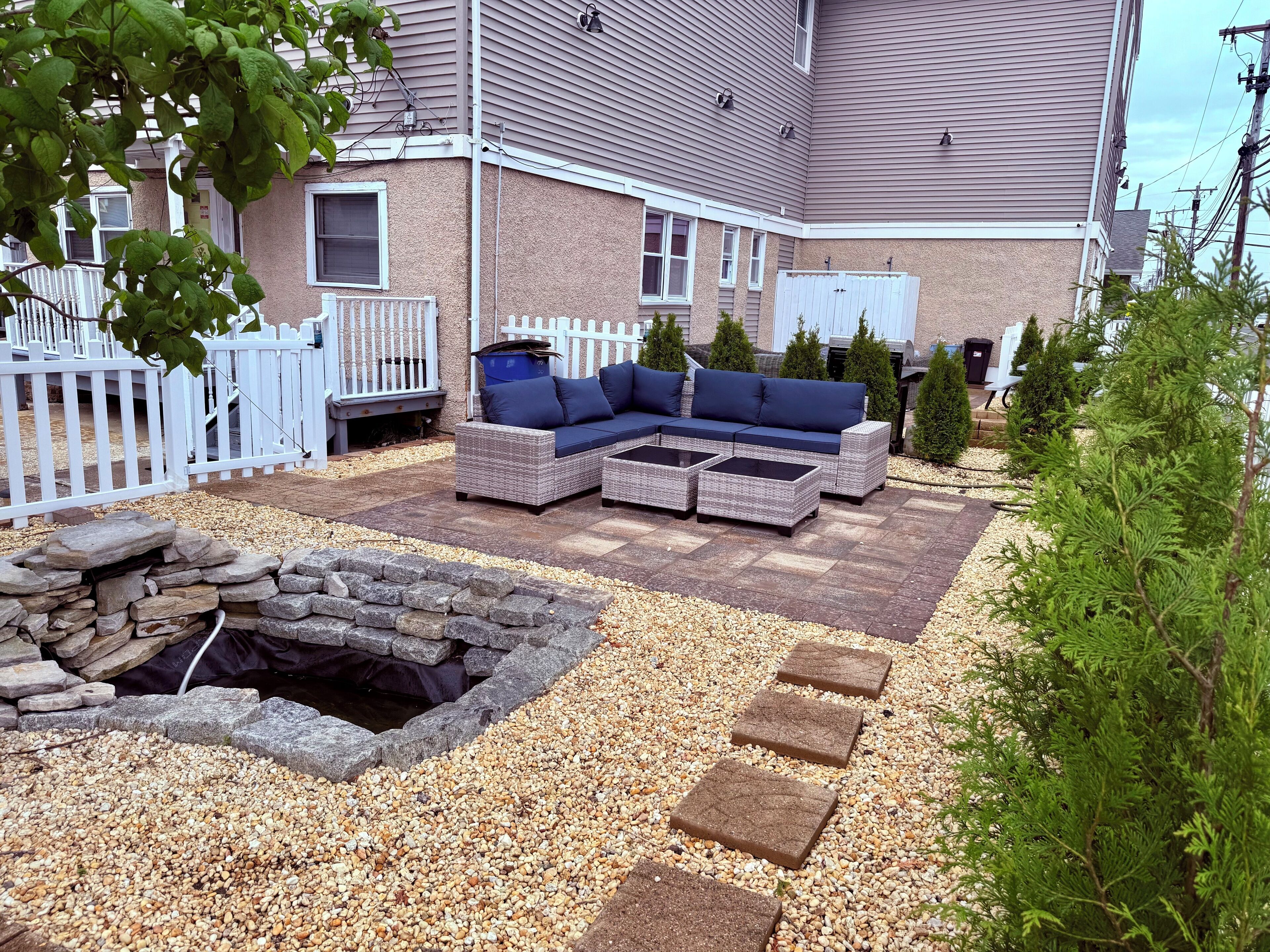 A patio area with outdoor furniture, a stone fire pit, and a white fence.