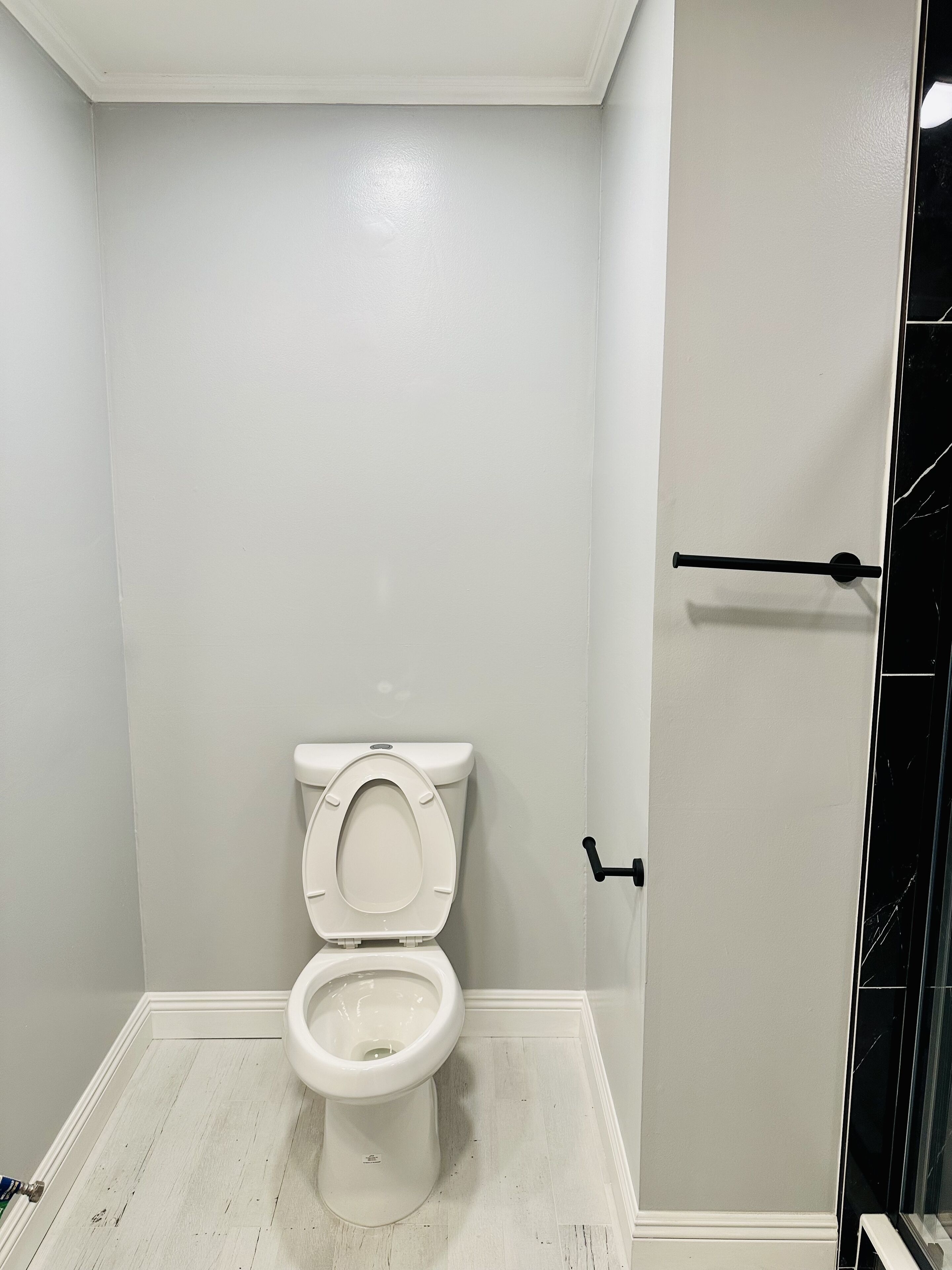 A small, clean bathroom with a white toilet, a white floor, and a door with a black handle.