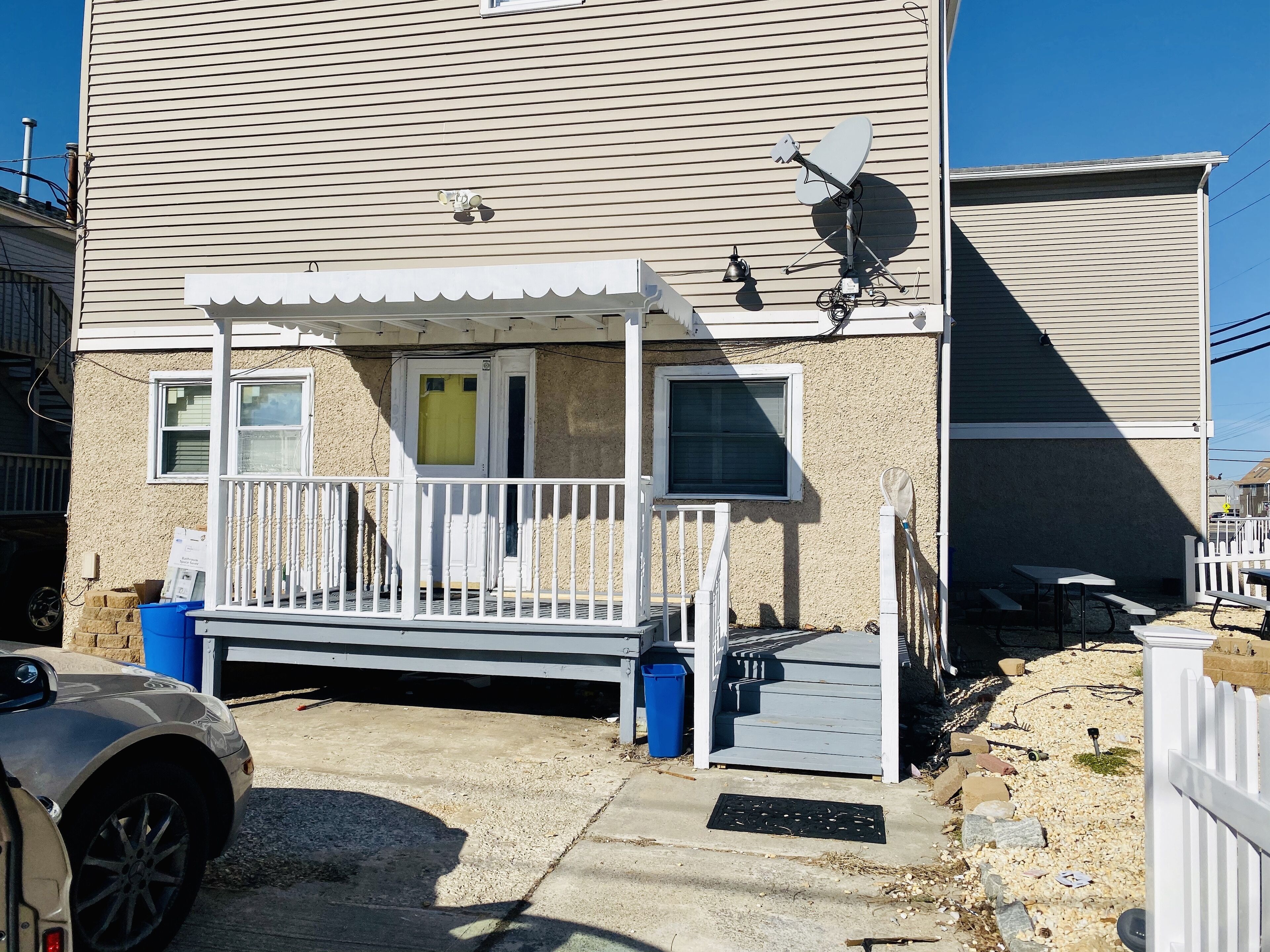 A two-story house with a covered porch, a satellite dish, and a small outdoor seating area.
