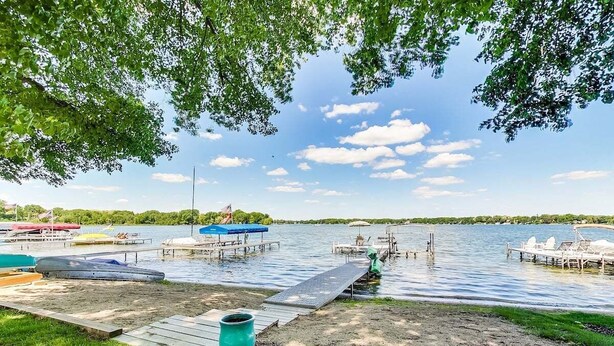 A lakeside dock with boats, a grassy area, and a clear sky. - Lake Daze | Lakefront Powers Lake Home, Sleeps 11 (Genoa City)