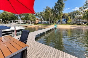 A wooden deck with a metal railing, a red umbrella, and a view of a calm water body with boats. - Lake Daze | Lakefront Powers Lake Home, Sleeps 11 (Genoa City)