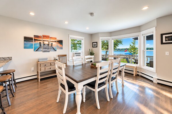 A dining area with a wooden table and chairs, a kitchen area with a counter and cabinets, and large windows with a view of the outdoors.