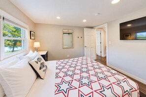Un dormitorio con cama, mesita de noche, espejo y puerta que da a otra habitación.