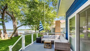 A deck with a sofa, a small table, and a striped umbrella. - Lake Daze | Lakefront Powers Lake Home, Sleeps 11 (Genoa City)