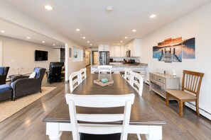 A spacious living area with a dining table, white chairs, a sofa, and a kitchen in the background. - Lake Daze | Lakefront Powers Lake Home, Sleeps 11 (Genoa City)