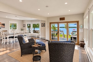 A spacious living area with a view of a lake, a dining set, and two wicker sofas. - Lake Daze | Lakefront Powers Lake Home, Sleeps 11 (Genoa City)