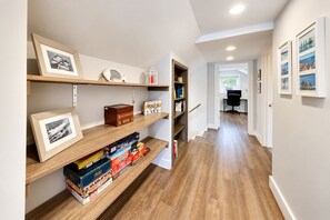 A hallway with wooden shelves displaying framed photos, board games, and a Monopoly box. - Lake Daze | Lakefront Powers Lake Home, Sleeps 11 (Genoa City)