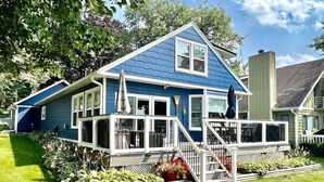 A two-story house with a blue exterior, white trim, and a covered front porch with a staircase. - Lake Daze | Lakefront Powers Lake Home, Sleeps 11 (Genoa City)