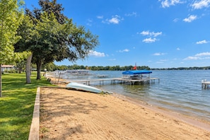 A lakeside dock with boats, a sandy beach, and a grassy area with trees. - Lake Daze | Lakefront Powers Lake Home, Sleeps 11 (Genoa City)