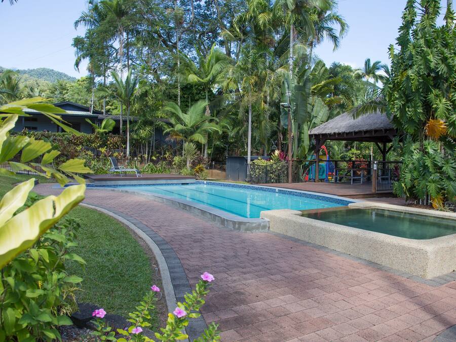 A pool area with a thatched-roof structure, surrounded by lush tropical vegetation and a mountain backdrop.