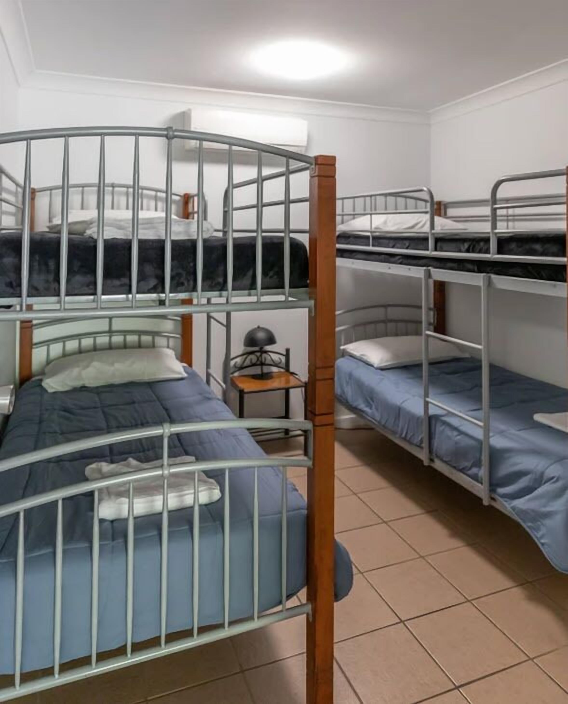 Une chambre de dortoir avec des lits superposés, une petite table avec une lampe et un sol carrelé.