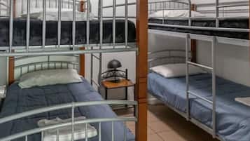 Une chambre de dortoir avec des lits superposés, une petite table avec une lampe et un sol carrelé.
