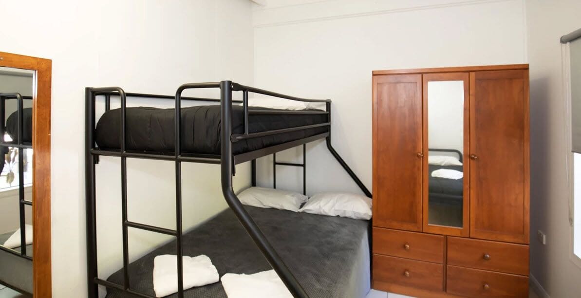 A bunk bed with a wooden wardrobe and a mirror.