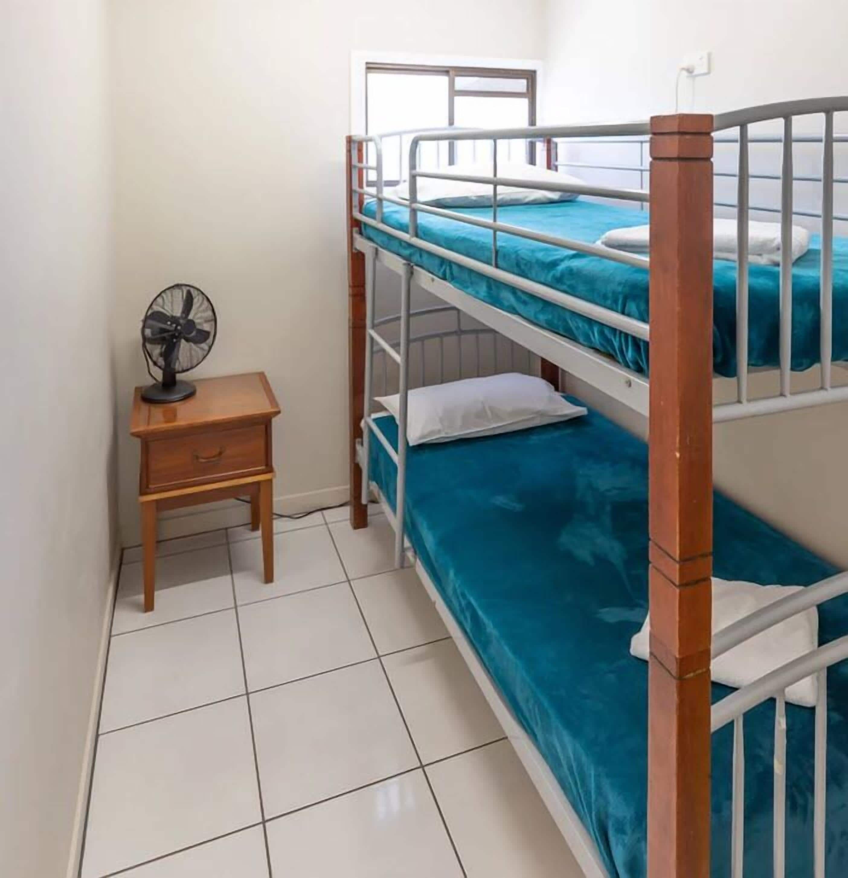 A bunk bed room with a wooden nightstand and a fan.