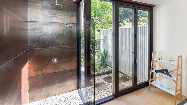 Un baño moderno con cabina de ducha de vidrio, un banco de madera y un estante pequeño con artículos de tocador.