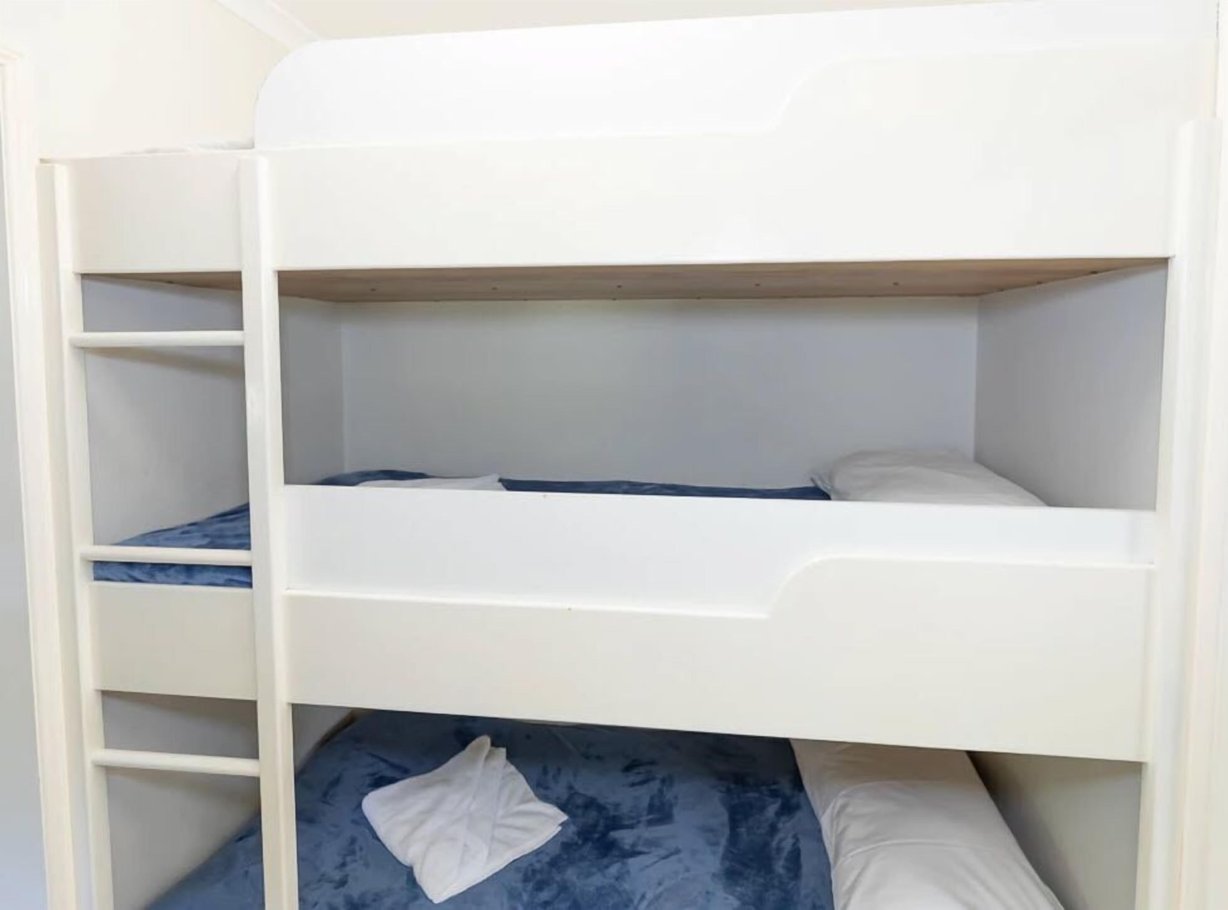 Un lit superposé à trois niveaux, chaque niveau étant équipé d’un matelas et d’oreillers.