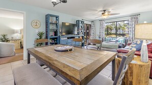 Ein geräumiges Wohnzimmer mit einem Holzesstisch, bequemen Sitzmöglichkeiten, einem Fernseher und einem Deckenventilator.