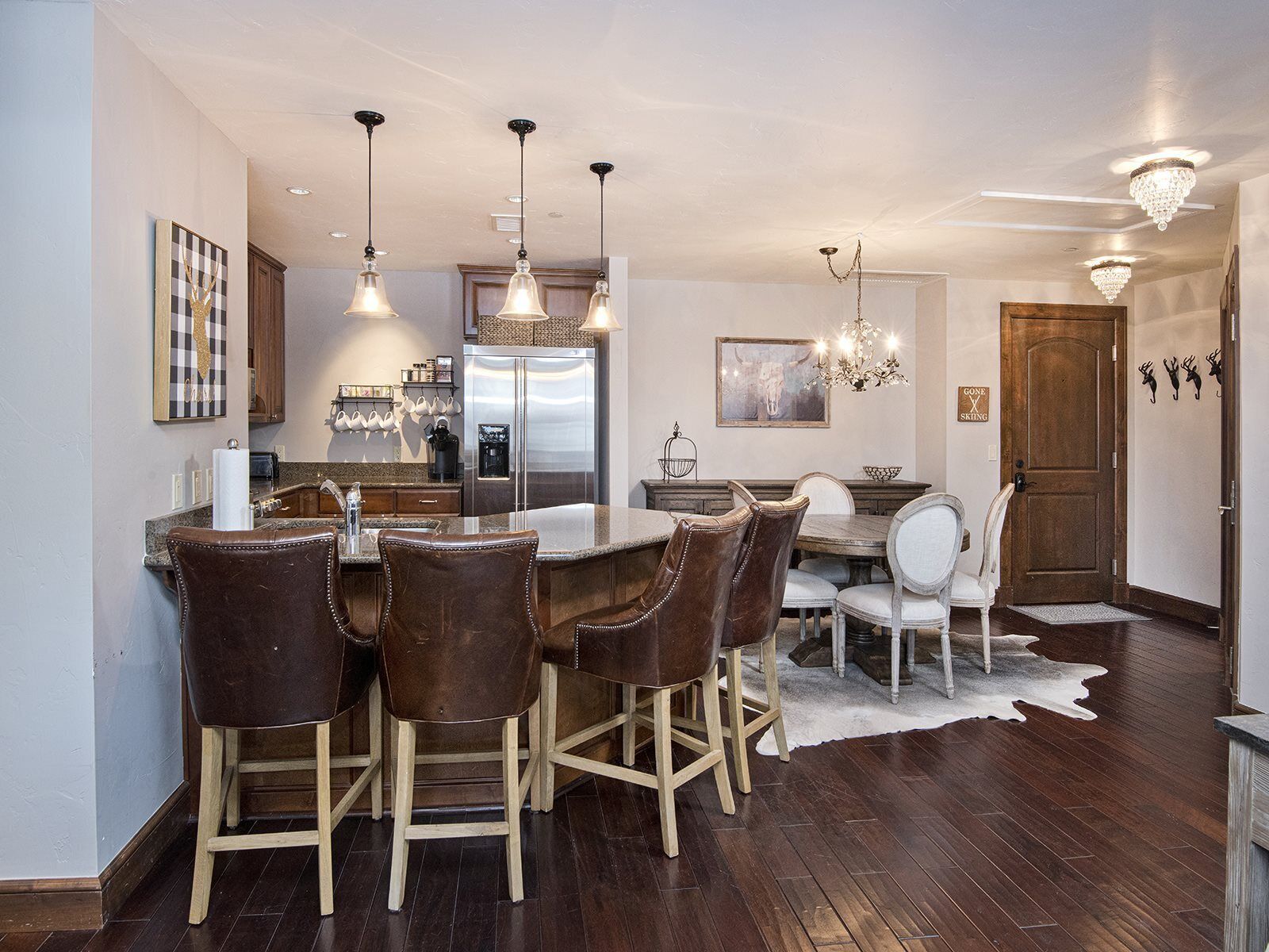 A modern kitchen with a central island, bar stools, pendant lighting, and a chandelier.
